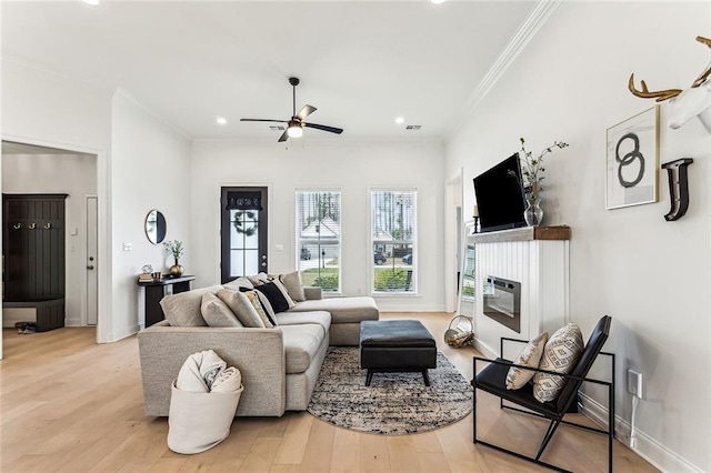 living room featuring a ceiling fan, baseboards, ornamental molding, light wood-style floors, and a glass covered fireplace