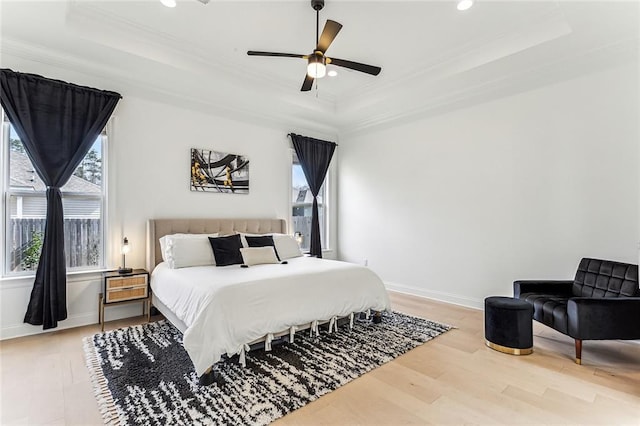 bedroom with baseboards, a tray ceiling, light wood-style flooring, recessed lighting, and crown molding