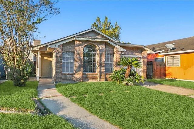 single story home featuring brick siding, a chimney, a front yard, and fence