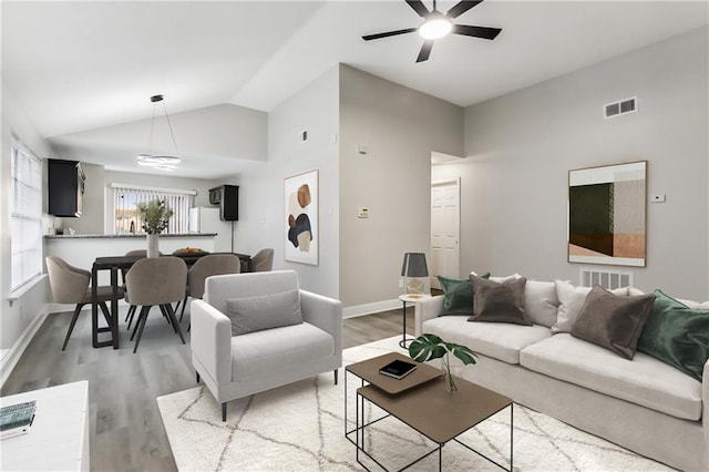 living area featuring light wood finished floors, visible vents, baseboards, and vaulted ceiling