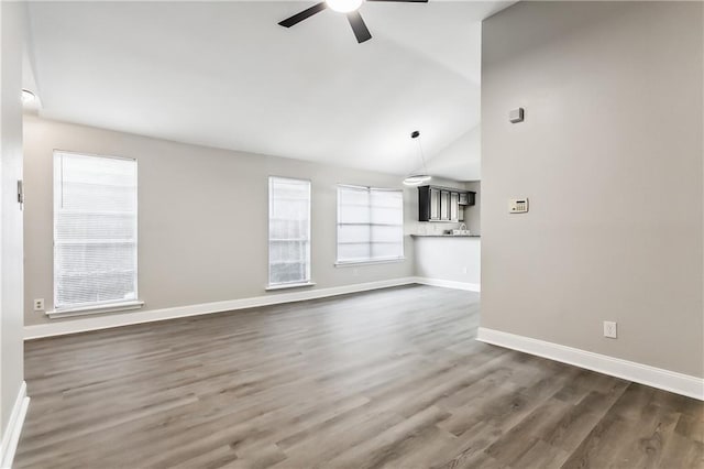 unfurnished living room featuring dark wood-style floors, ceiling fan, lofted ceiling, and baseboards