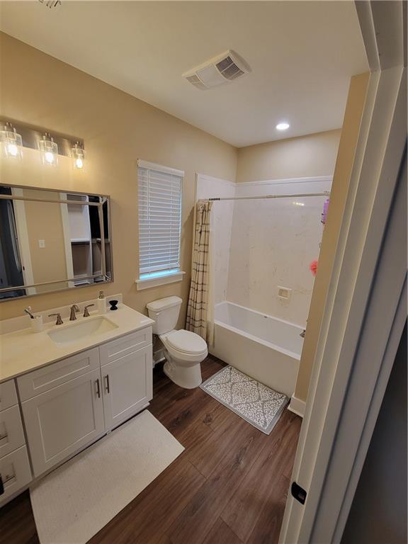 bathroom featuring visible vents, toilet, shower / tub combo with curtain, wood finished floors, and vanity