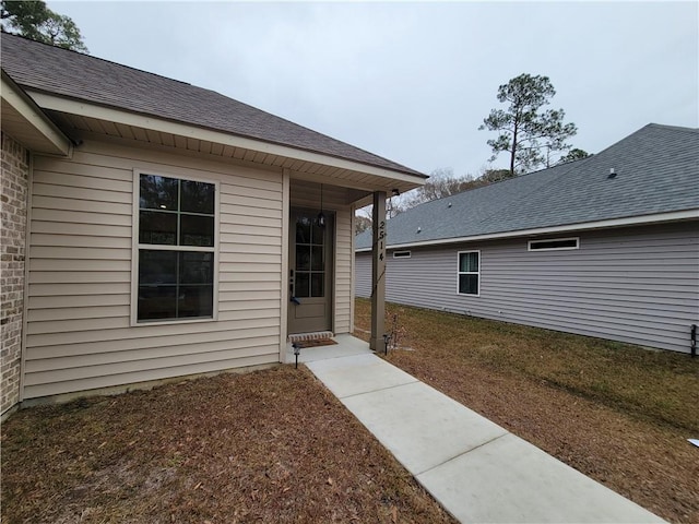 view of exterior entry featuring brick siding and roof with shingles