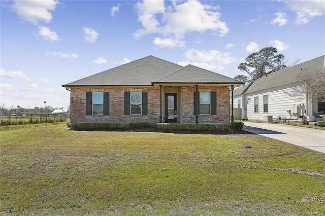 view of front of home with brick siding, roof with shingles, concrete driveway, and a front yard