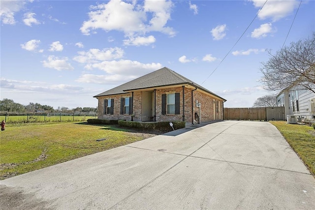 view of front of property with brick siding, fence, concrete driveway, central AC, and a front yard