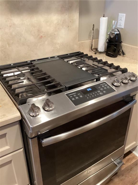 details featuring stainless steel gas range oven, white cabinetry, light countertops, and wood finished floors