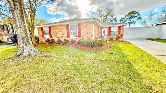 view of front facade featuring brick siding, driveway, a front yard, and fence