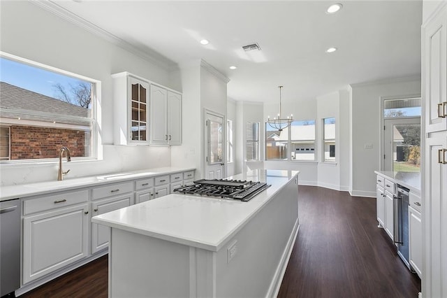 kitchen with ornamental molding, a sink, stainless steel appliances, an inviting chandelier, and white cabinets