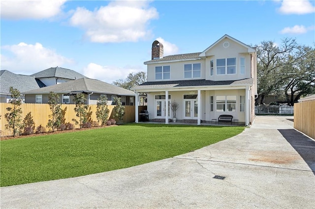 view of front facade with stucco siding, driveway, fence, french doors, and a front yard