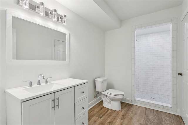 bathroom featuring vanity, wood finished floors, baseboards, a tile shower, and toilet