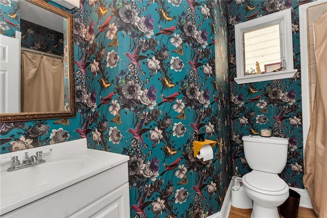 full bathroom with wallpapered walls, toilet, vanity, and baseboards