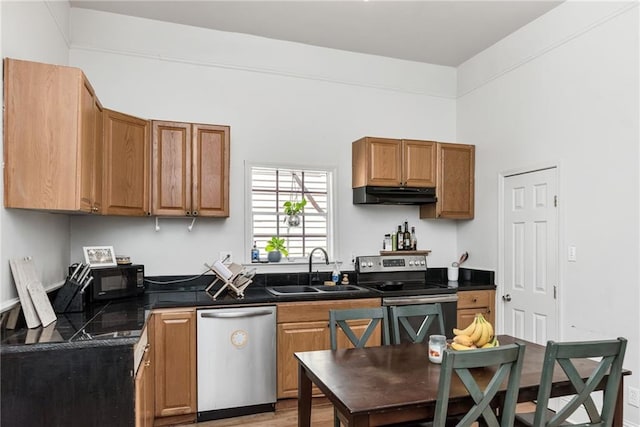 kitchen featuring brown cabinets, a sink, under cabinet range hood, dark countertops, and appliances with stainless steel finishes