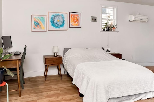 bedroom featuring a wall mounted air conditioner, baseboards, and light wood-style flooring