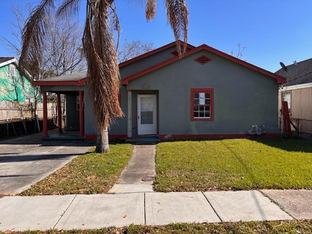 view of front facade featuring an attached carport, fence, concrete driveway, a front yard, and stucco siding