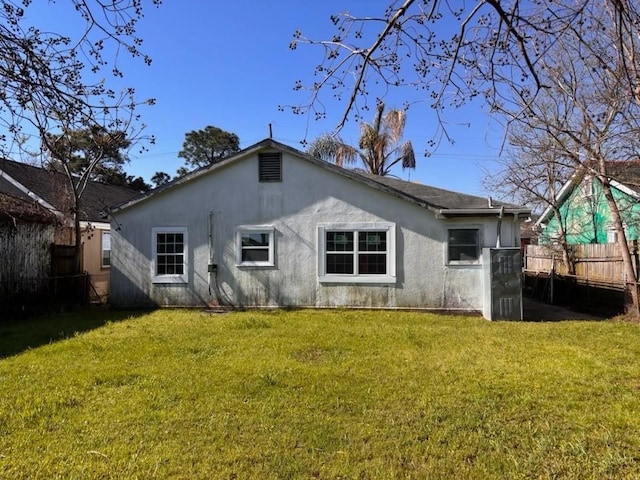 rear view of house with a lawn, fence, and stucco siding