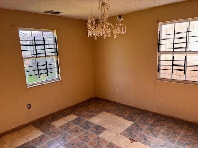 spare room featuring visible vents, baseboards, a textured ceiling, and a chandelier