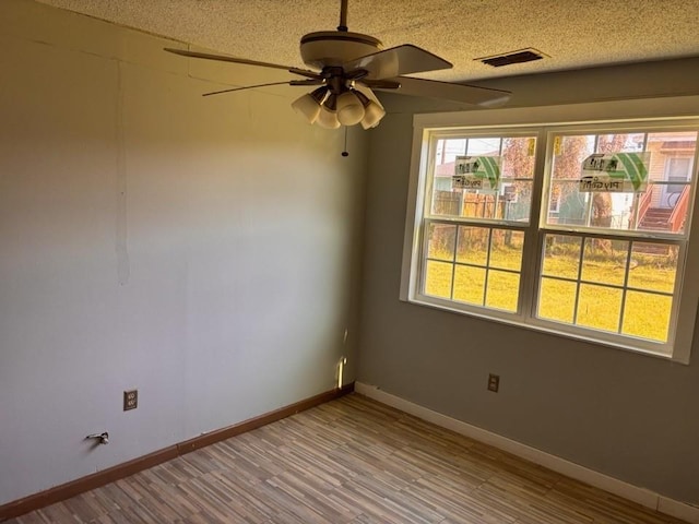 unfurnished room featuring visible vents, a textured ceiling, wood finished floors, baseboards, and ceiling fan