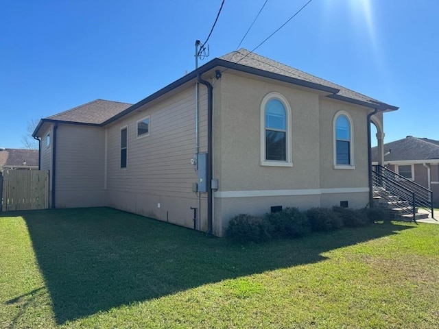 view of home's exterior with crawl space, a lawn, a shingled roof, and fence