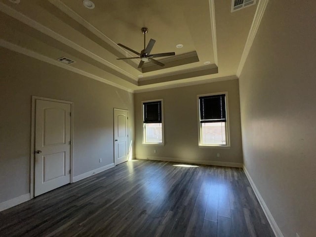 spare room featuring visible vents, dark wood-type flooring, ceiling fan, a tray ceiling, and ornamental molding