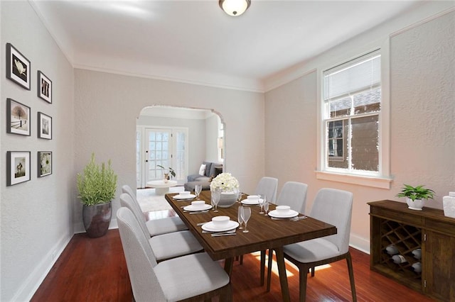 dining space featuring baseboards, wood finished floors, arched walkways, and a healthy amount of sunlight