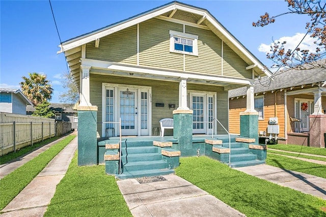 shotgun-style home featuring french doors, covered porch, a front yard, and fence