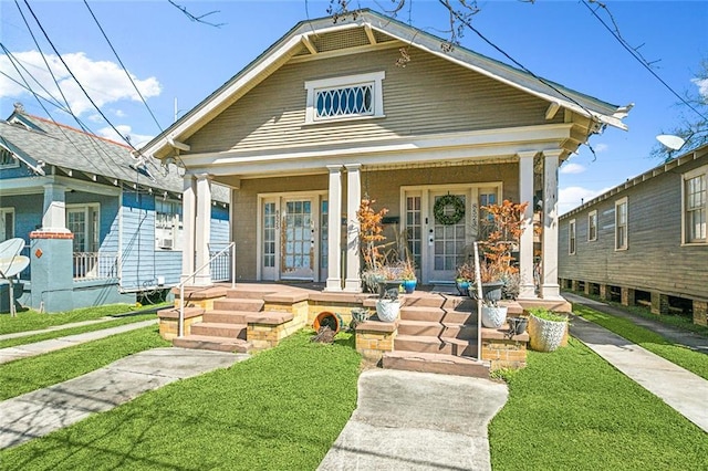 shotgun-style home with covered porch, french doors, and a front lawn