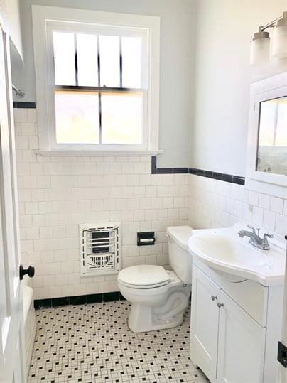 bathroom with tile walls, a wainscoted wall, toilet, heating unit, and vanity