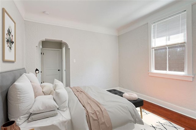 bedroom featuring crown molding, baseboards, wood finished floors, a textured wall, and arched walkways