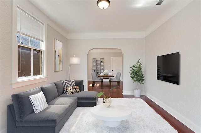 living room with baseboards, visible vents, arched walkways, dark wood-type flooring, and crown molding