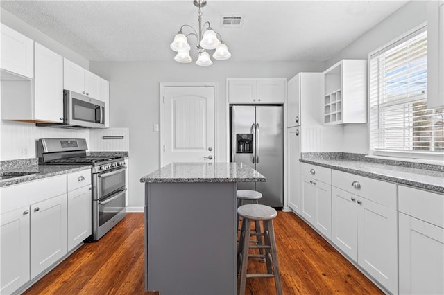 kitchen with visible vents, a kitchen bar, a notable chandelier, dark wood finished floors, and appliances with stainless steel finishes