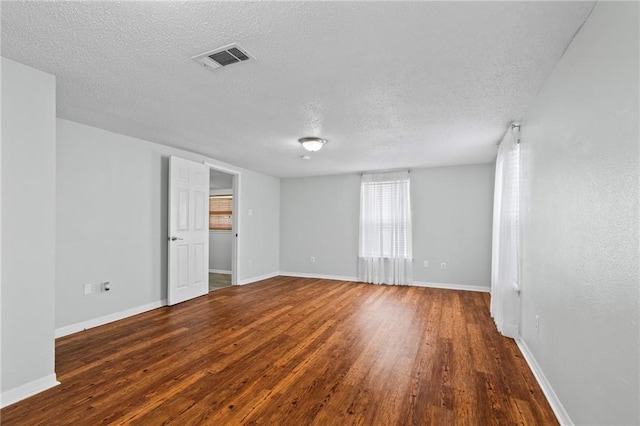 spare room with a textured ceiling, wood finished floors, visible vents, and baseboards