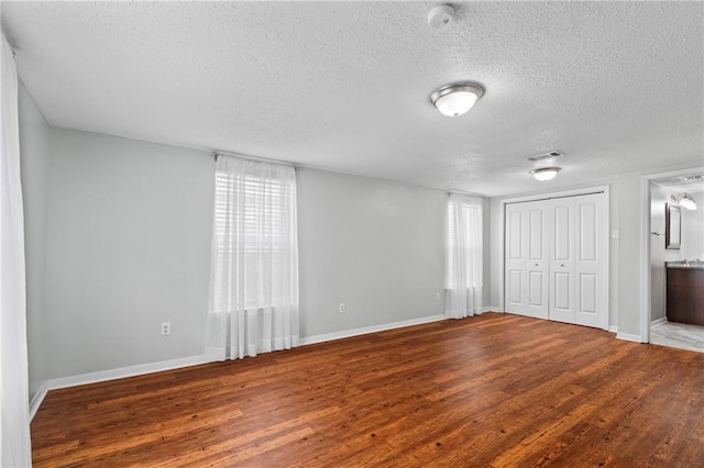 unfurnished bedroom with multiple windows, wood finished floors, visible vents, and baseboards