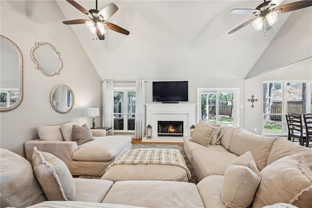 living area featuring high vaulted ceiling, a lit fireplace, and a ceiling fan