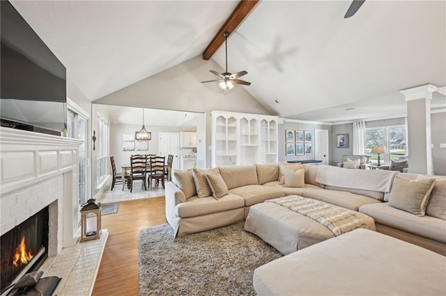 living room featuring light wood finished floors, high vaulted ceiling, beam ceiling, a fireplace, and ceiling fan