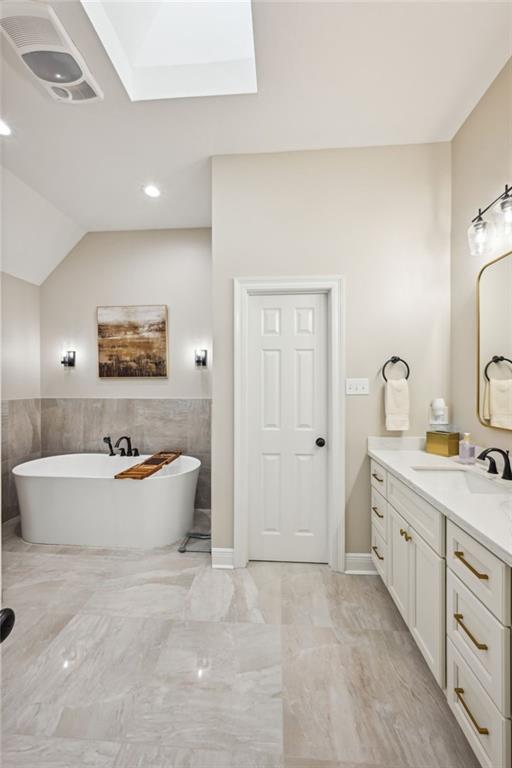 full bathroom featuring vanity, a soaking tub, marble finish floor, and lofted ceiling with skylight