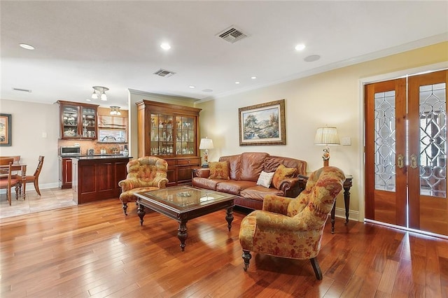 living area featuring visible vents, light wood-style flooring, and crown molding