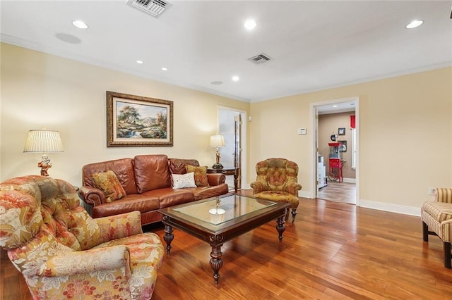 living area with crown molding, wood finished floors, visible vents, and baseboards