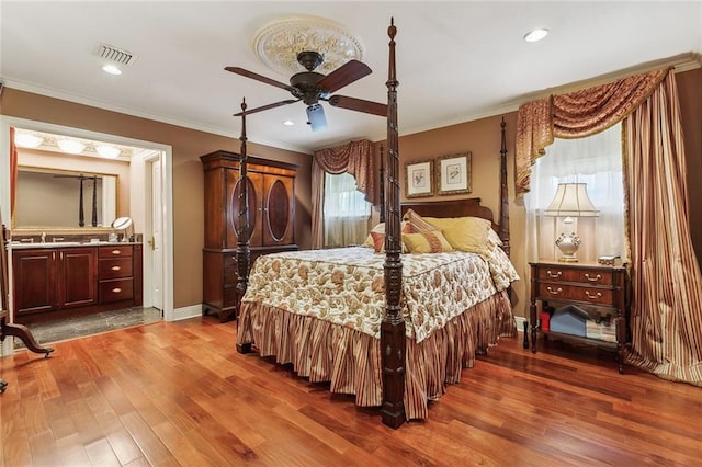 bedroom featuring visible vents, a sink, wood finished floors, crown molding, and baseboards