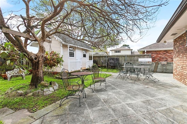 view of patio with outdoor dining space, an outbuilding, fence, and grilling area