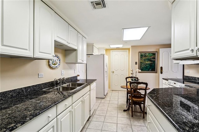 kitchen featuring white appliances, light tile patterned floors, visible vents, a sink, and white cabinets