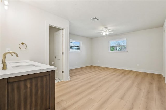 interior space with visible vents, a ceiling fan, a sink, wood finished floors, and baseboards