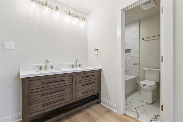 bathroom featuring double vanity, marble finish floor, toilet, and a sink