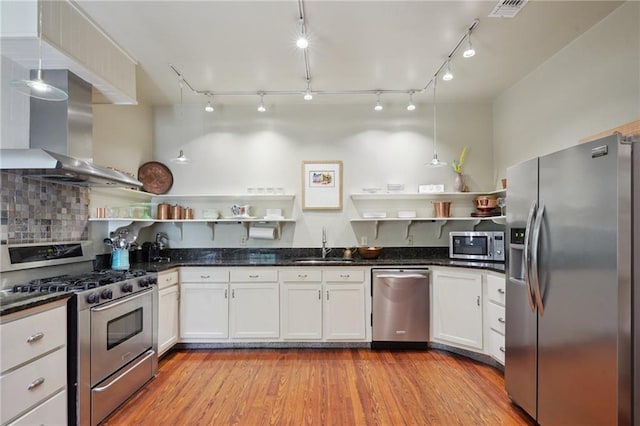 kitchen with open shelves, appliances with stainless steel finishes, a sink, and wall chimney range hood