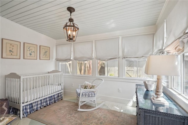 bedroom with baseboards, a nursery area, an inviting chandelier, and ornamental molding