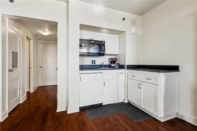 kitchen with dark countertops, visible vents, dark wood-type flooring, black microwave, and white cabinetry