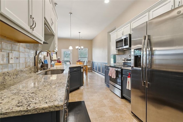 kitchen featuring a sink, appliances with stainless steel finishes, wainscoting, white cabinetry, and a chandelier