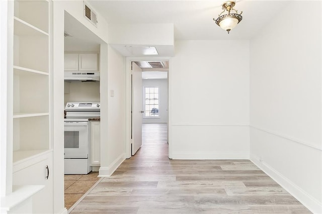 hall with light wood-type flooring, visible vents, and baseboards