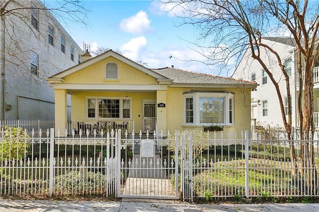 bungalow-style house with a fenced front yard, brick siding, covered porch, and a gate