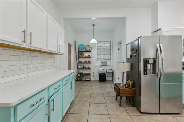 kitchen with light tile patterned floors, hanging light fixtures, stainless steel fridge, white cabinets, and tasteful backsplash