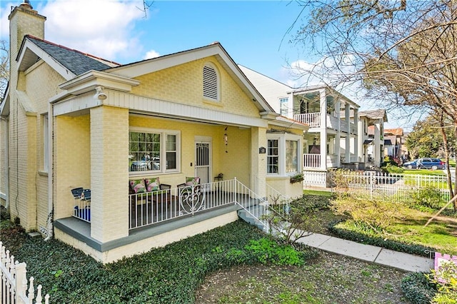 view of front of house with a porch, a balcony, fence, brick siding, and a chimney